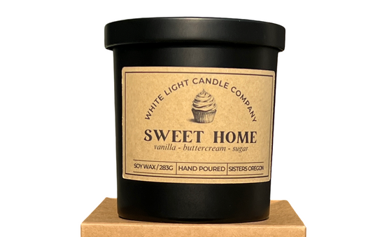 Black candle with 'Sweet Home' label on a matching cardboard box, both featuring the White Light Candle Company branding.