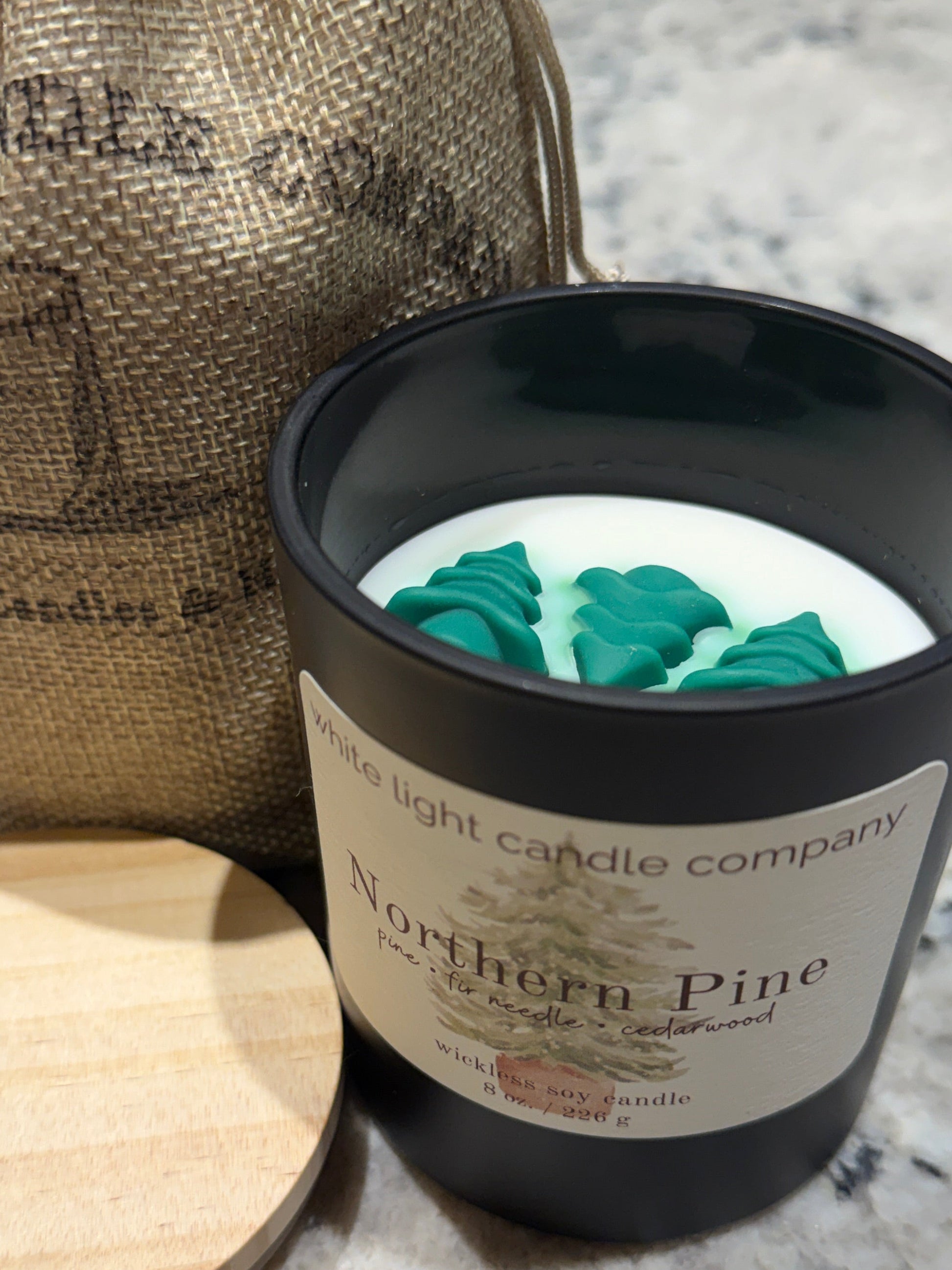 Candle in a black container with a wooden lid on a marble surface