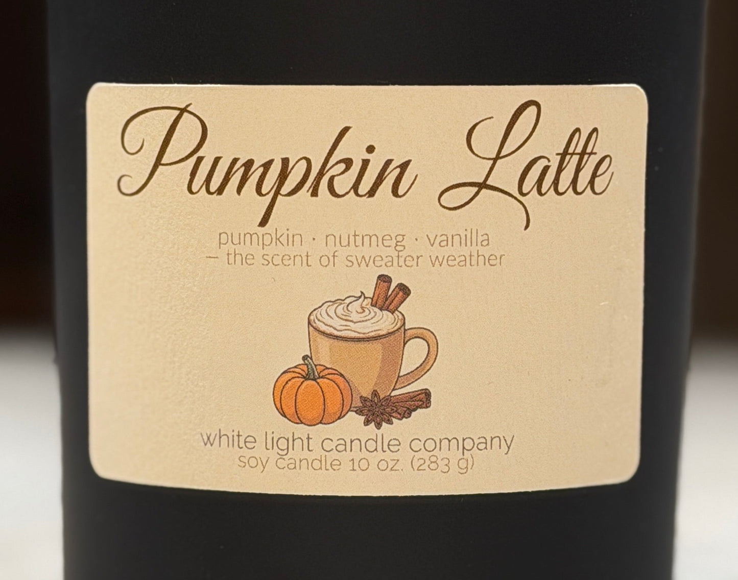 Black candle labeled 'Pumpkin Latte' on a marble surface with a blurred background