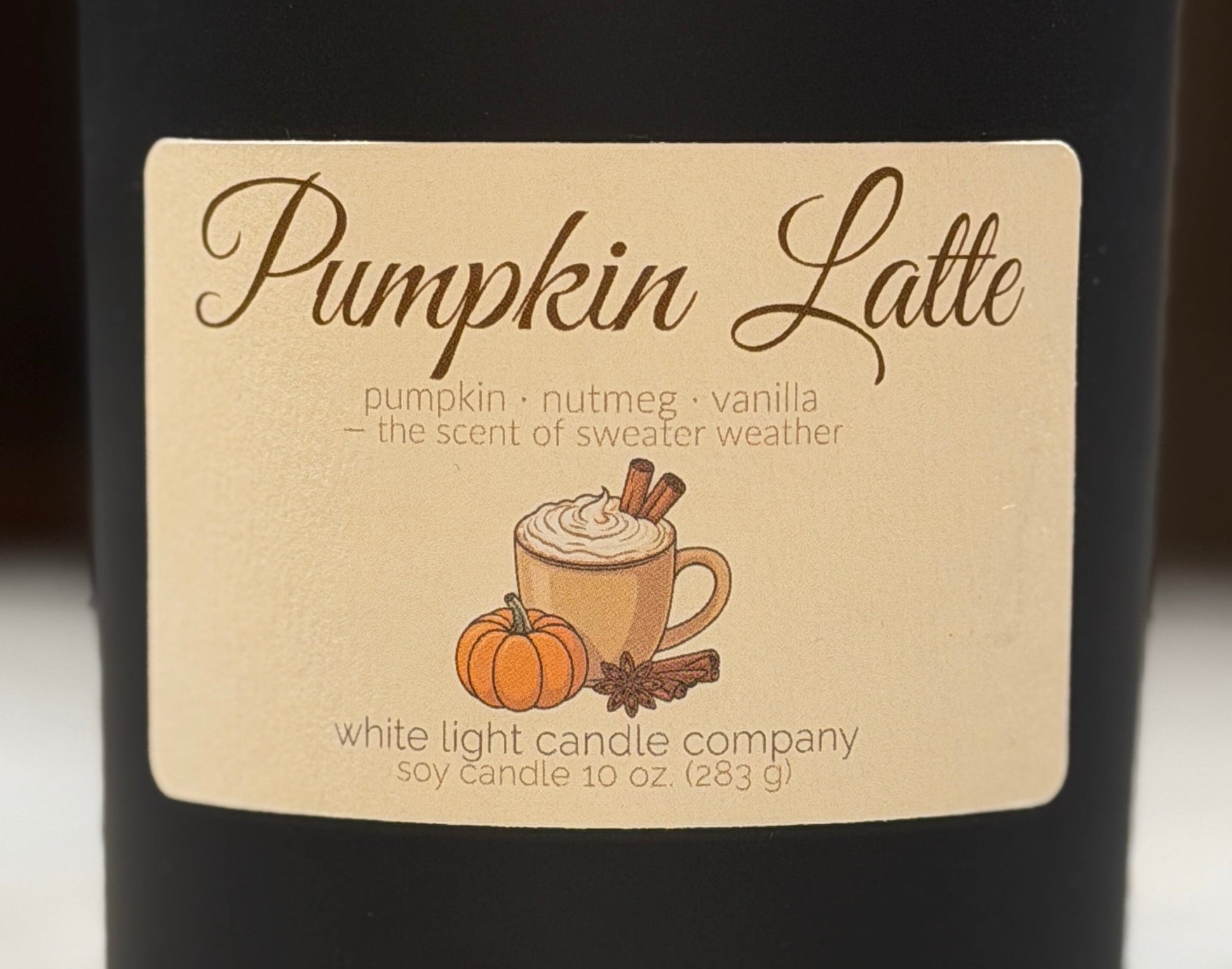 Black candle labeled 'Pumpkin Latte' on a marble surface with a blurred background
